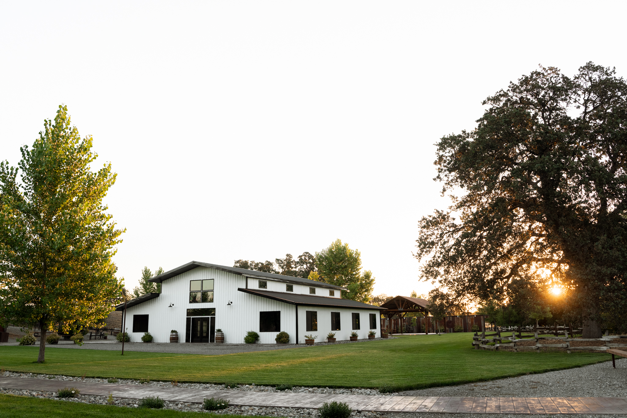 The white barn at The Crossing on Thomes Creek with the sun setting through the valley oaks
